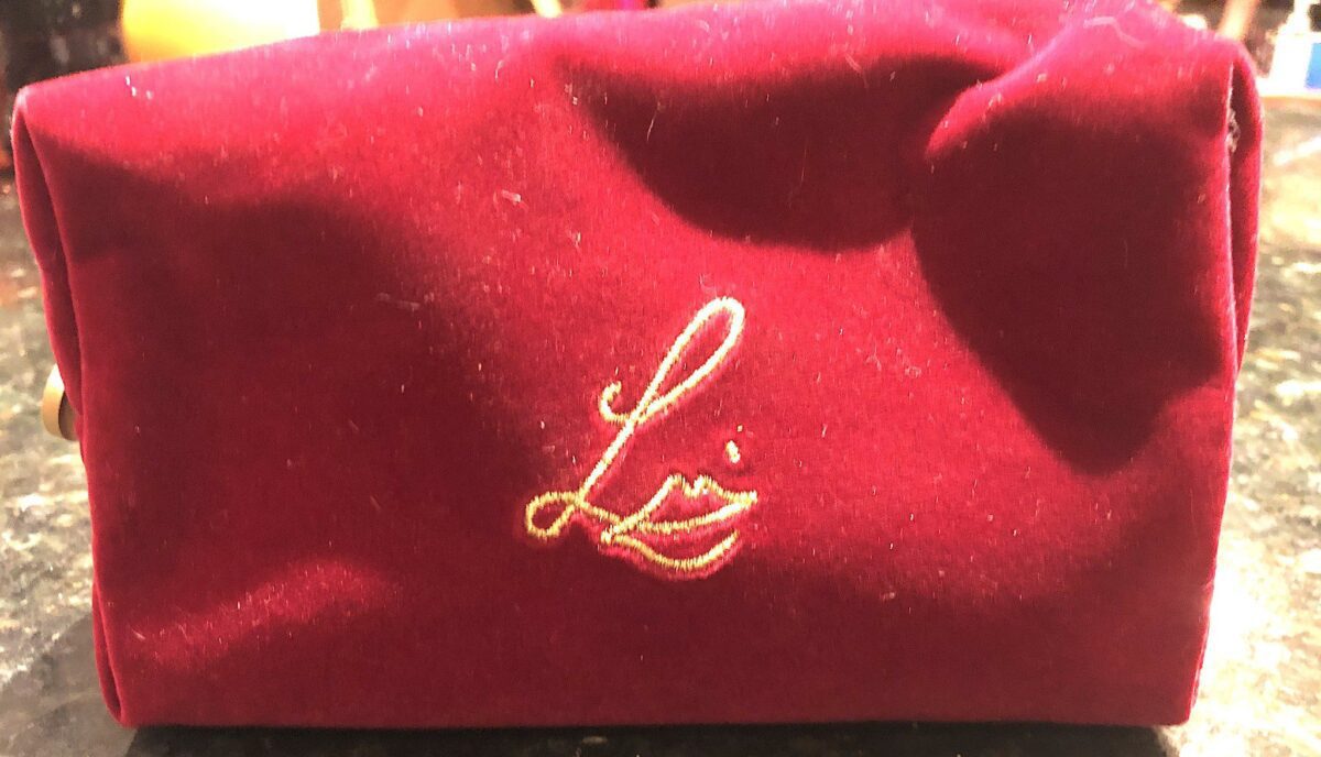 THE SIGNATURE LOGO IS ON ONE SIDE OF THE CHERRY VELVET MAKEUP POUCH